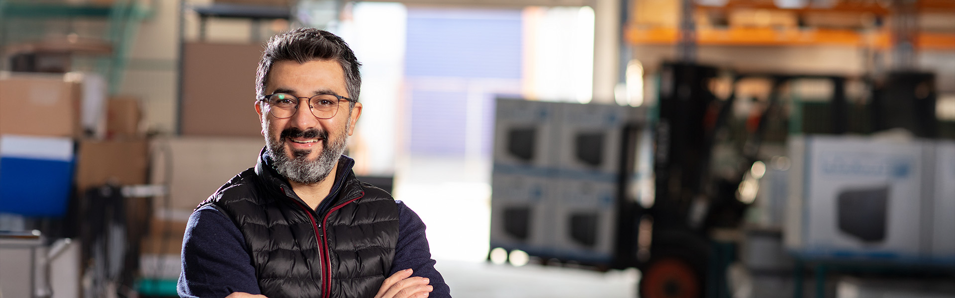 Man with glasses smiling at camera in a warehouse