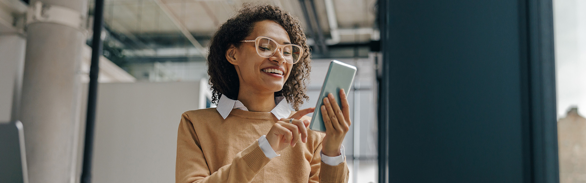 Smiling business woman is using phone in office near window